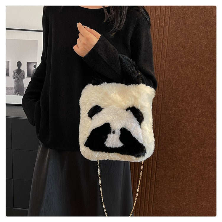 Person holding a panda-shaped bag with a chain strap in front of a brown wall.