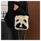 Person holding a panda-shaped bag with a chain strap in front of a brown wall.